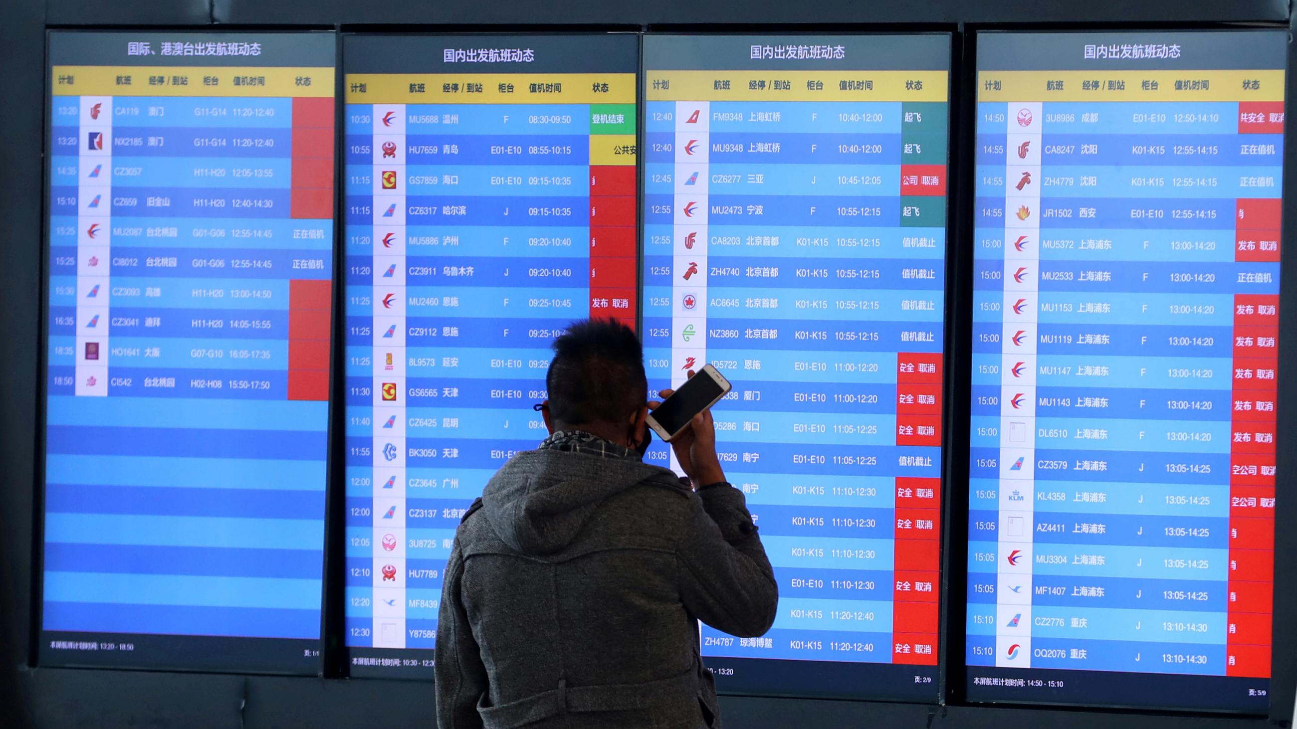 A man stands in front of an airport screen showing multiple flight departure cancellations after the city was locked down following the outbreak of a new coronavirus in Wuhan, China on Jan 23, 2020. 
