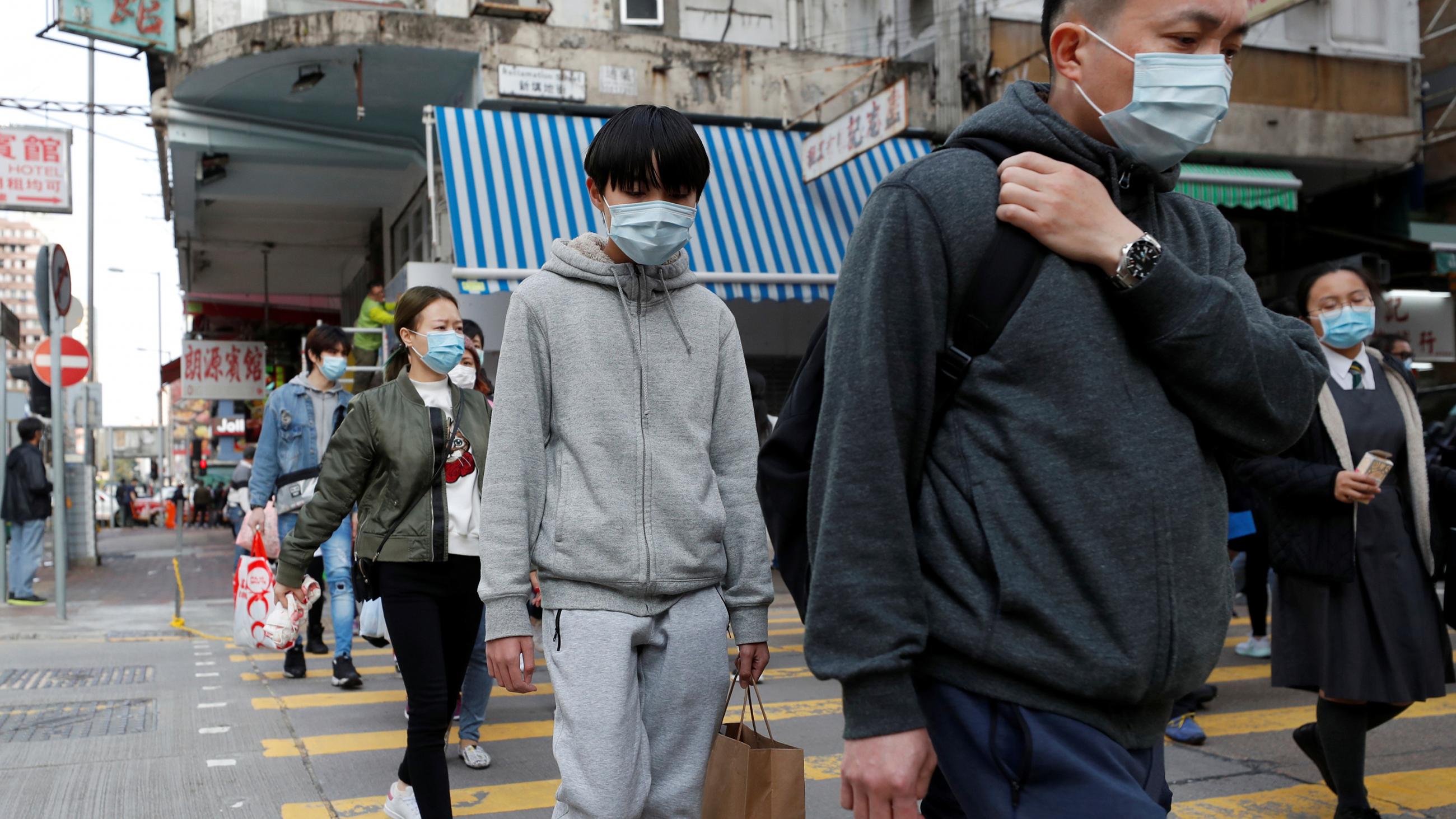 Photo shows a busy street in a shopping district with a number of people walking by the camera, all of whom are wearing masks. 
