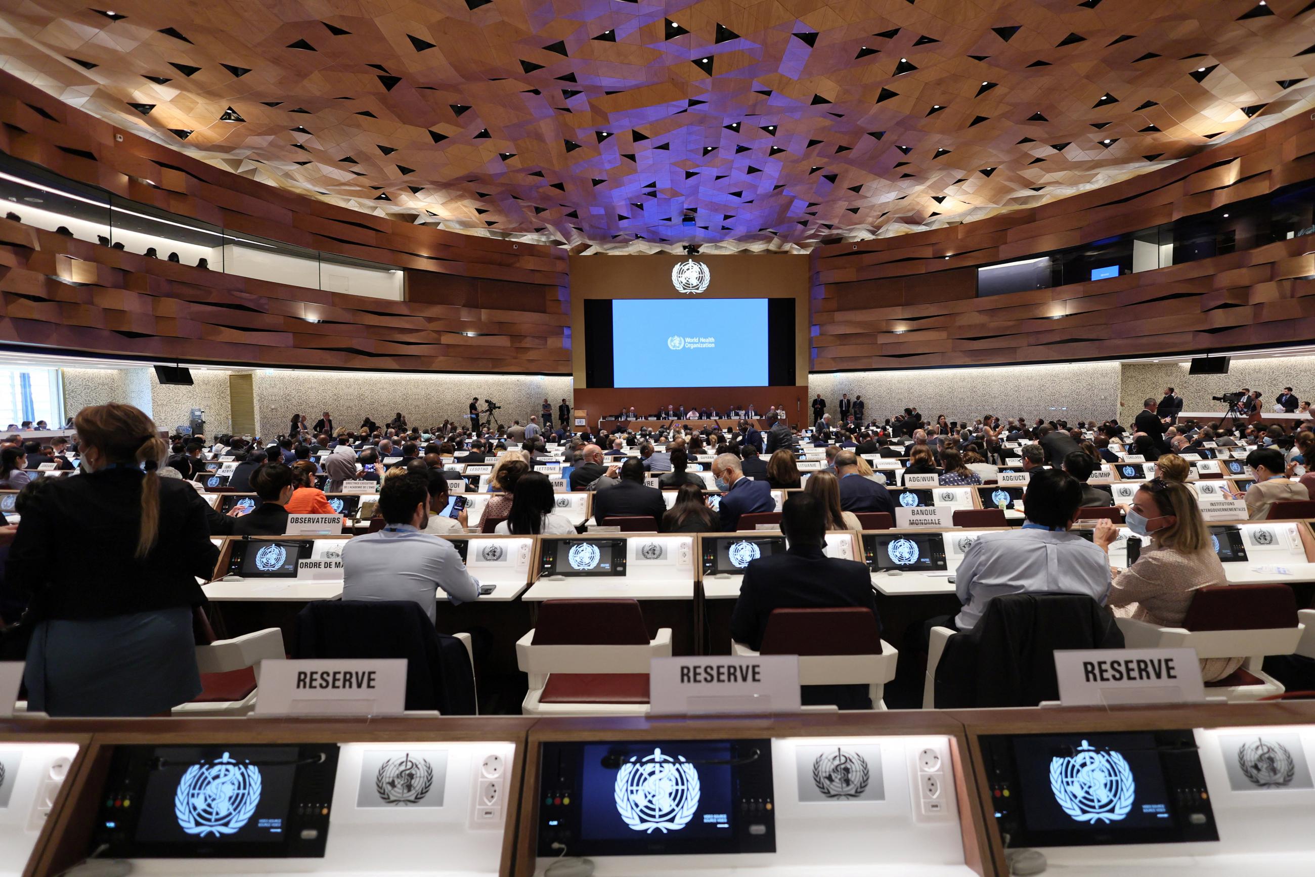 A view from the back of an expansive assembly hall where attendees are seated in rows at the 75th World Health Assembly meeting at the United Nations in Geneva, Switzerland, on May 22, 2022. 