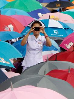 A nurse at a rally in Bangkok, Thailand. She stands among a sea of brightly colored umbrellas wearing a traditional nurse's uniform and facing the camera taking a picture in the direction of the viewer