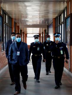 The picture shows three officers in full uniforms and two officials wearing suits walking toward the camera down a long air terminal corridor with windows on both sides.