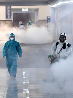 The photo shows several people clad head-to-toe in protective suits fogging what is presumably a disinfectant in thick clouds. 