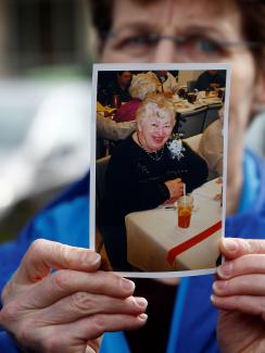 The image shows pat holding a picture of her mother partially in front of her face. Even though her face is partly obscured, Pat looks very distraught. Elaine in the photo is smiling warmly. This is a powerful and sad photo. 