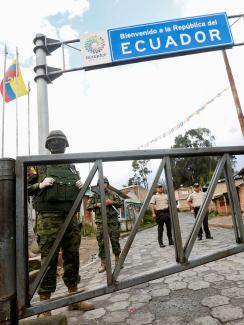 The photo shows a border crossing with a large sign reading, Ecuador, and several soldiers in the frame. 