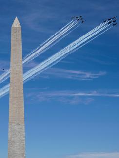 The photo shows two tight formations of several jets flying by the Washington monument on a brilliant blue sky day. 