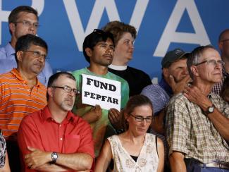 An audience member holds up a "Fund PEPFAR" sign during President Barack Obama's speech at a campaign event at Herman Park in Boone, Iowa, on August 13, 2012. 