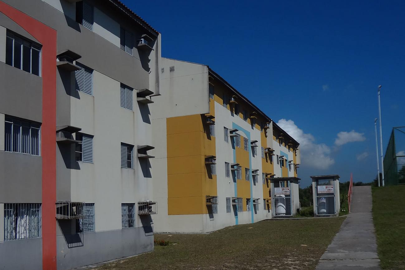 An apartment in the large urban center of Manaus, Brazil, showing a plain building with orange-beige and buttercream accents against a brilliant blue sky