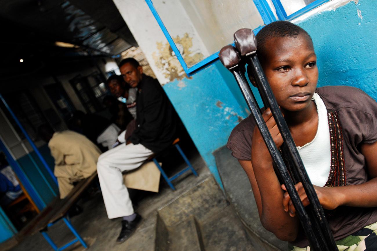 She is seen leaning against her crutches outside an open door to the clinic. 