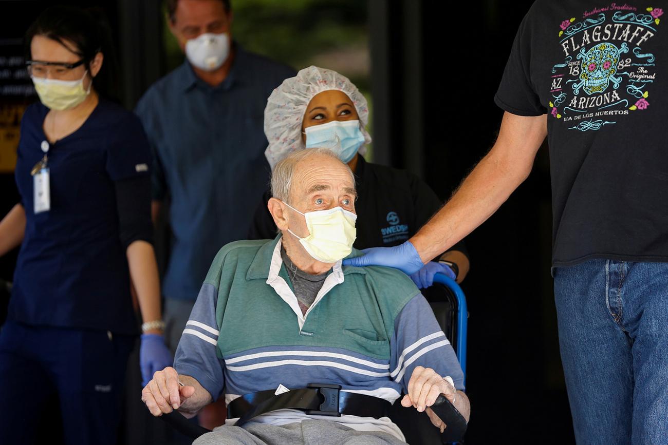 The photo shows Gene wearing a mask being wheeled by a health worker with his sons walking beside the wheelchair. 