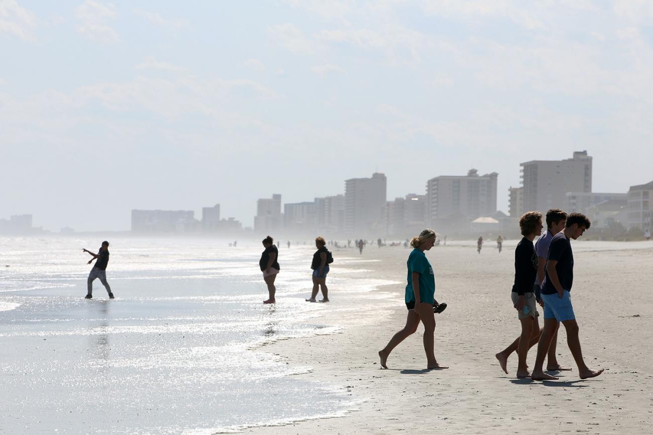 The photo shows people walking on the beach in what appears to be the early morning hours. 