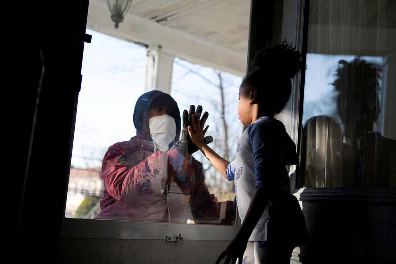 Picture shows the father on one side of the glass holding his hand up, and his daughter places her hand on the glass in response. 