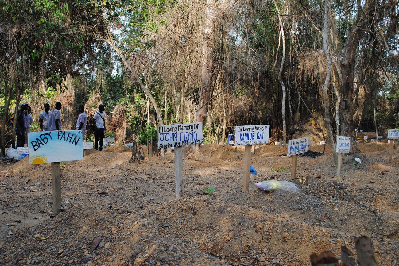 The graveyard has what appear to be freshly dug graves adorned with hand-painted wooden markers with names like "John Flomo" And "Baby Fahn." 