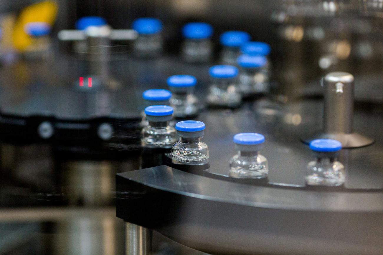 VPicture shows small vials with blue caps snaking down a robotic assembly line. 