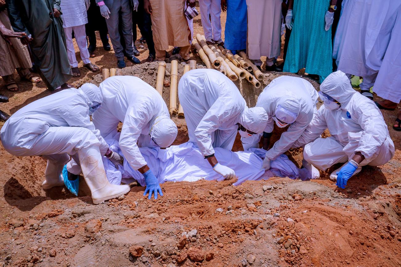 The photo shows people in protective gear lowering a body into the ground. 