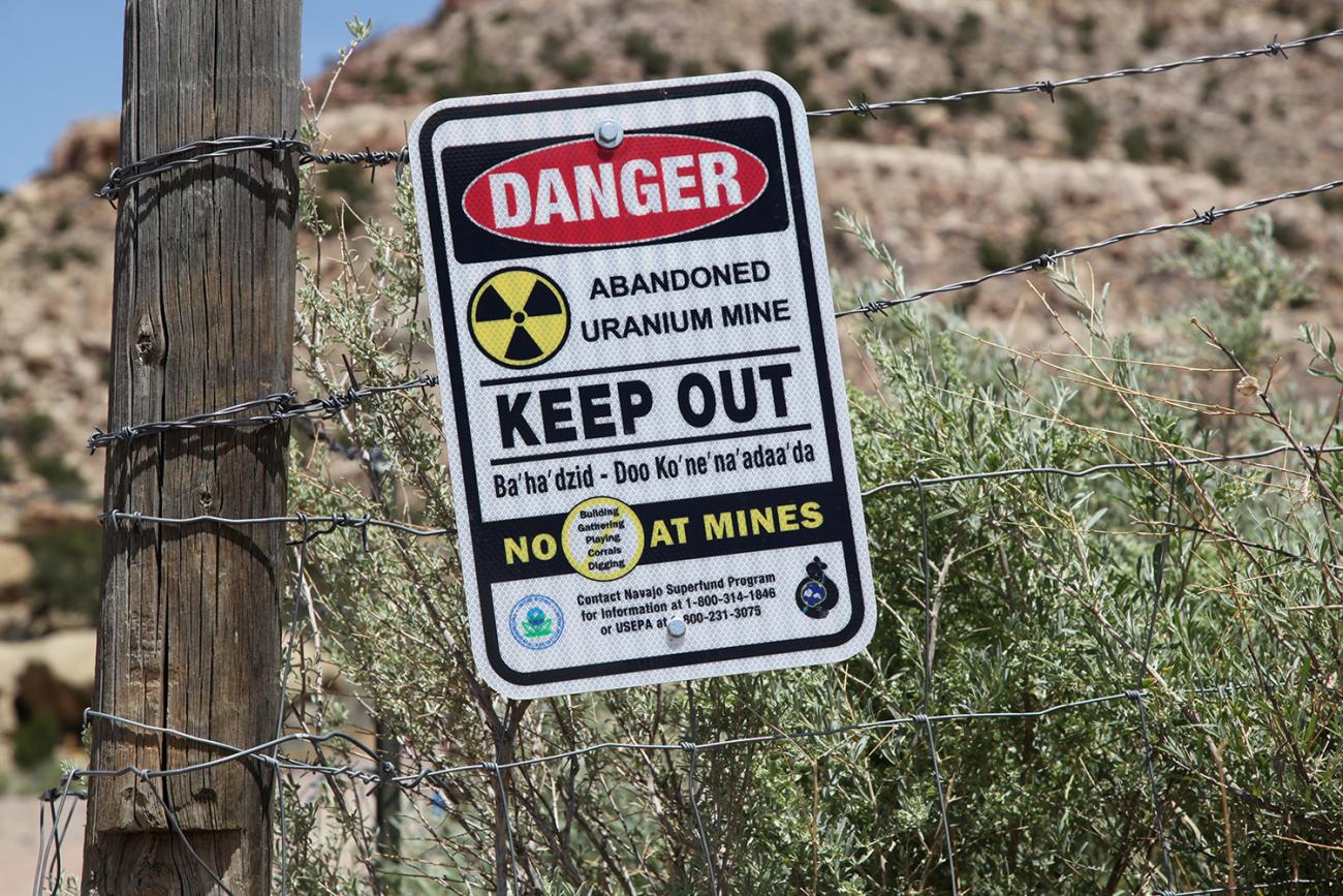 Picture shows a sign on a fence in a remote-looking desert area warning people to "KEEP OUT" because of the dangers. 