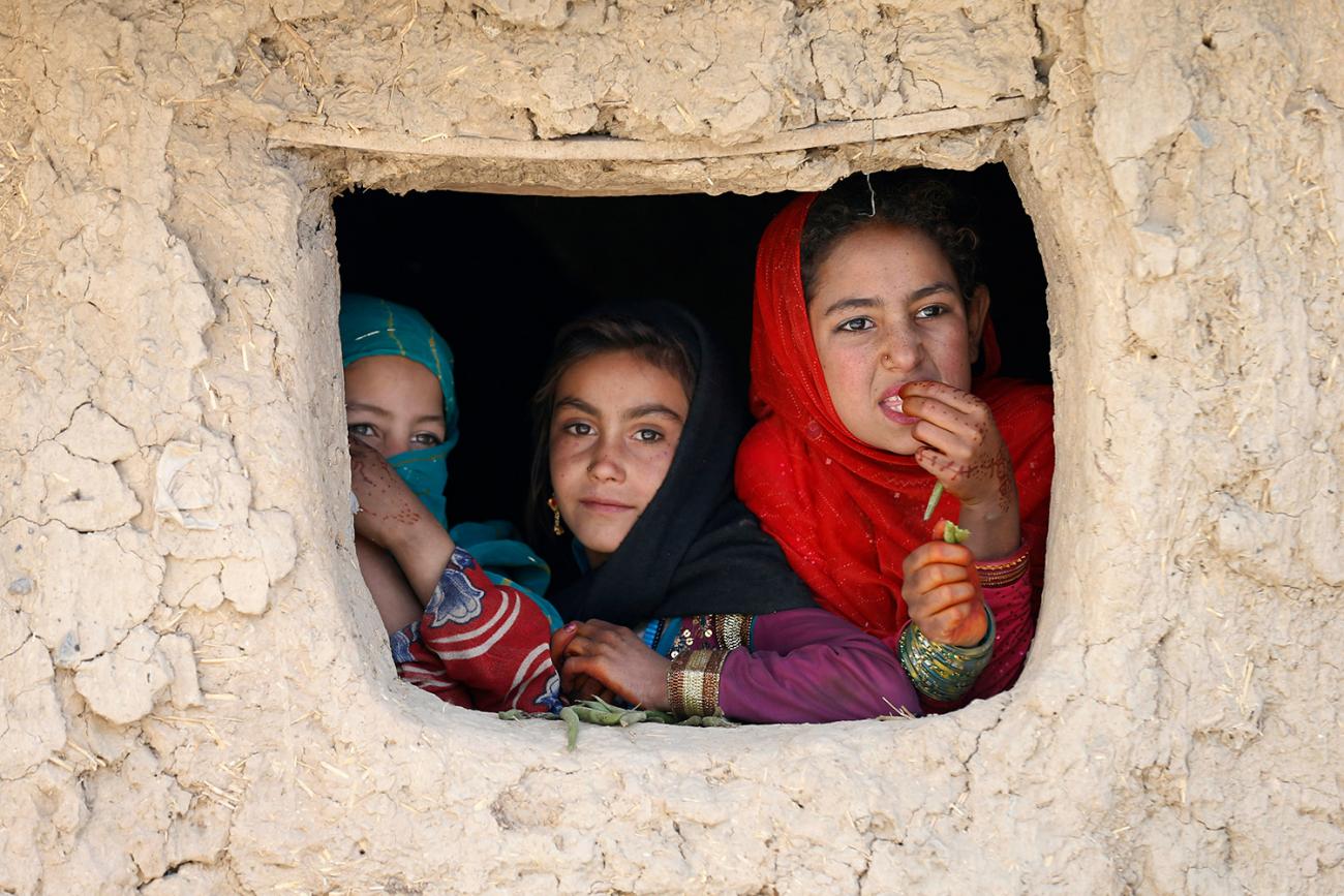 The photo shows three girls looking out the window of a building. 