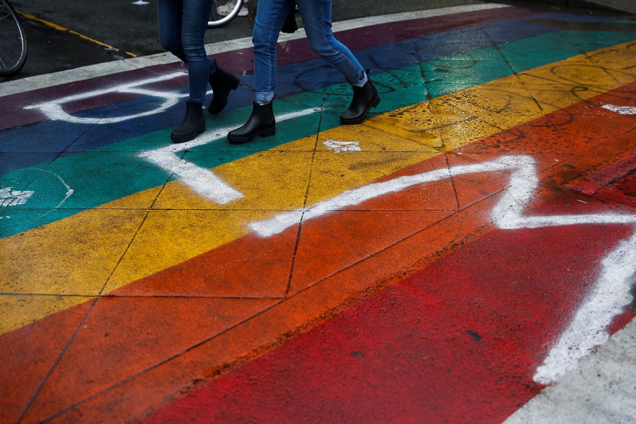Picture shows boots marching over a rainbow-painted section of street adorned with spray paint reading "BLM." 