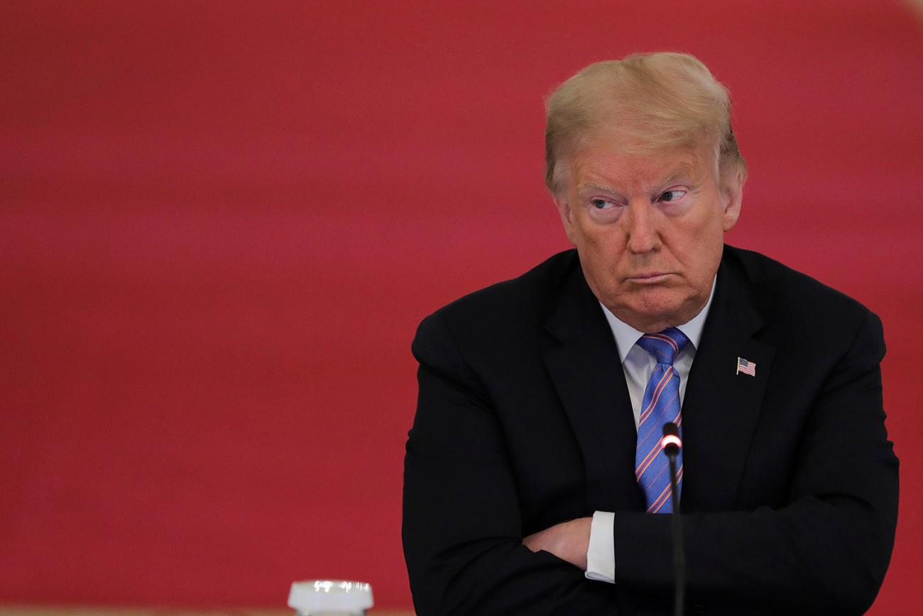 The photo shows the president with a harrumph look on his face, armed crossed, against a red backdrop. 