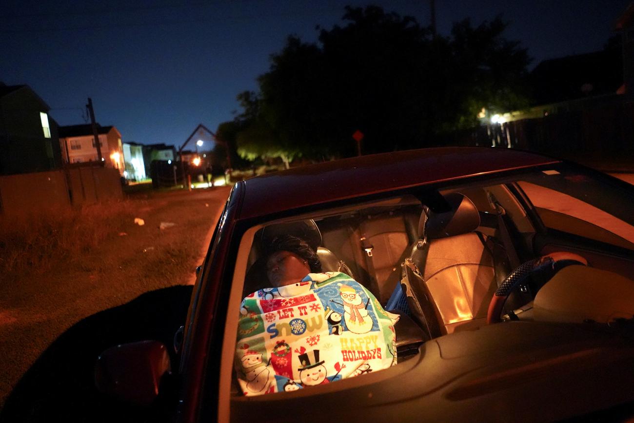 Picture shows the woman reclined in the passenger seat of her car at night. The glow from her phone illuminates her face. 