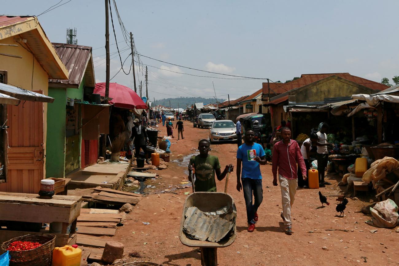 The photo shows a number of people on the street, including a man pushing an empty wheelbarrow. 