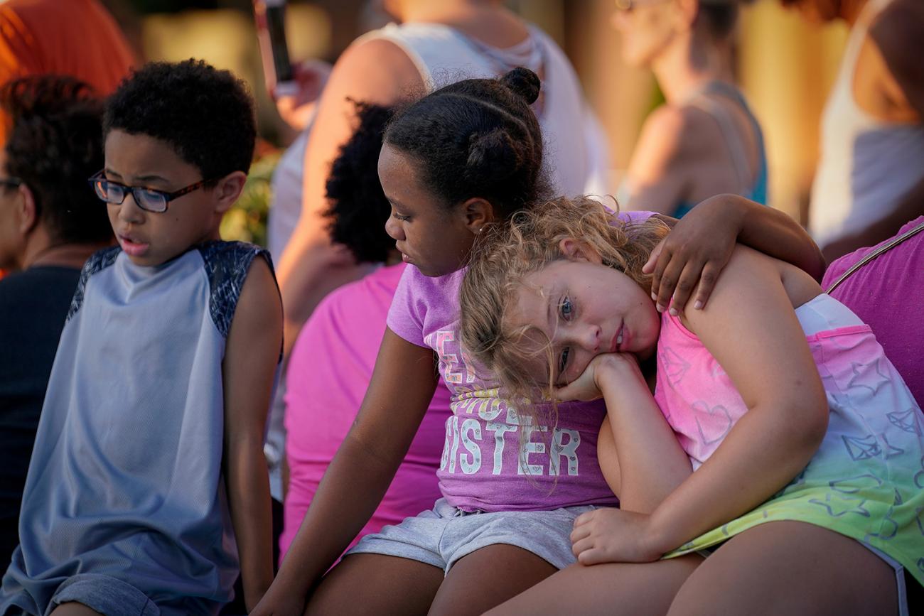 The photo shows a row of children seated and leaning on one another. 