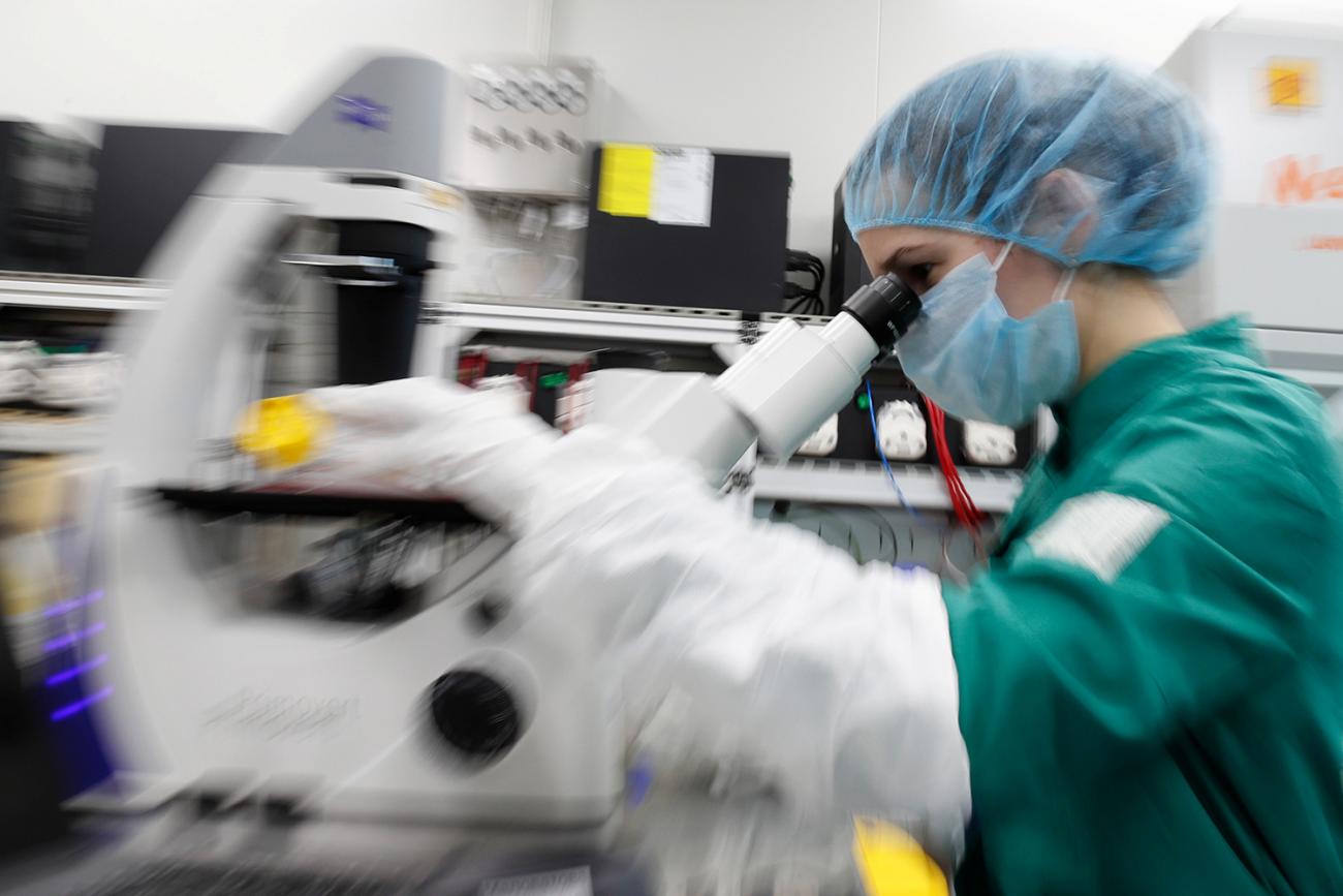 The photo shows a researcher in protective gear looking under a microscope