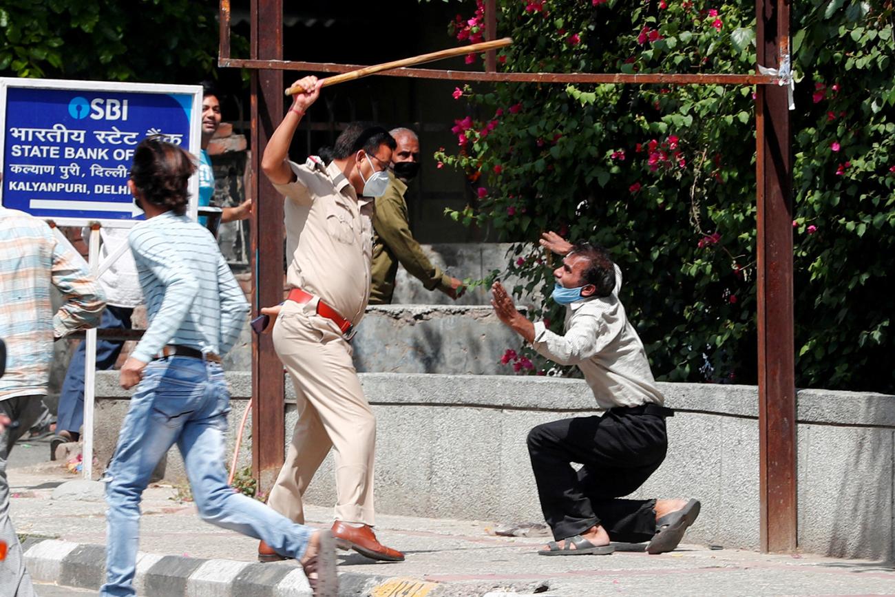 The photo shows a man on his knees appearing to plead with a uniformed officer who has a long baton raised high above his head ready to strike. 