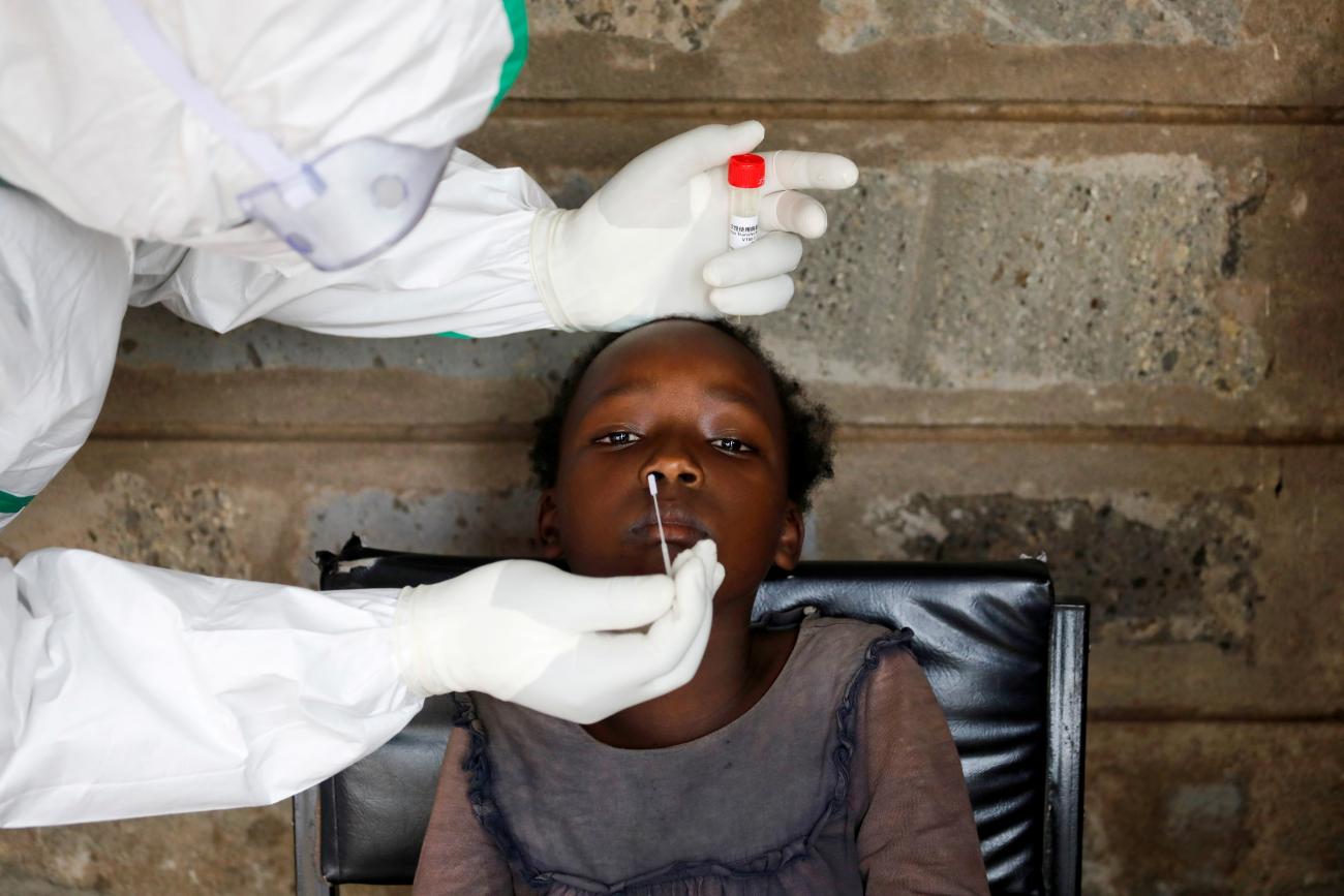 The photo shows a worker in full protective gear swabbing the nose of a girl. 