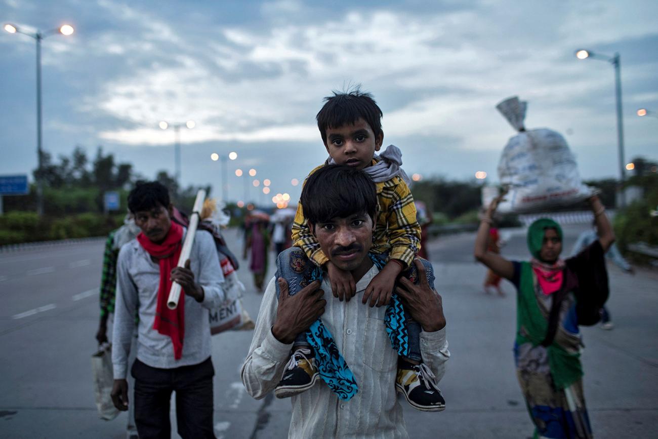 The photo shows a man with a boy on his shoulders walking with others on a road at dusk. 