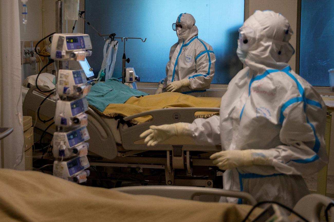 Picture shows two health workers in full uniforms attending to patients in beds. 