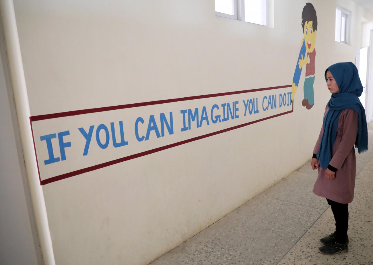 Fatima Noori, 15, looks at writing on a school wall as she arrives to attend psychotherapy class two weeks after a massive bomb exploded outside her school killing at least 80 students. Photo taken in Kabul, Afghanistan, on May 26, 2021. 