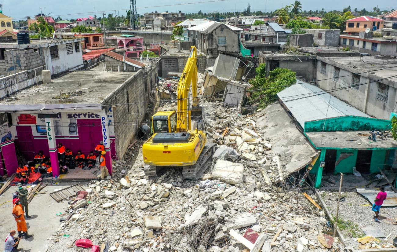 Members of a Mexican rescue team take a break as a backhoe removes the rubble of a collapsed house a week after an earthquake battered Les Cayes, Haiti. Photo taken August 21, 2021.