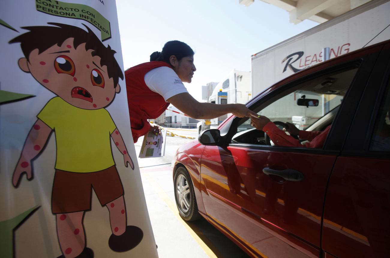 Spurred by measles outbreaks in California and Arizona, a health worker hands out measles prevention leaflets at the Ciudad Juarez, Mexico-El Paso, Texas, border on February 16, 2015. 