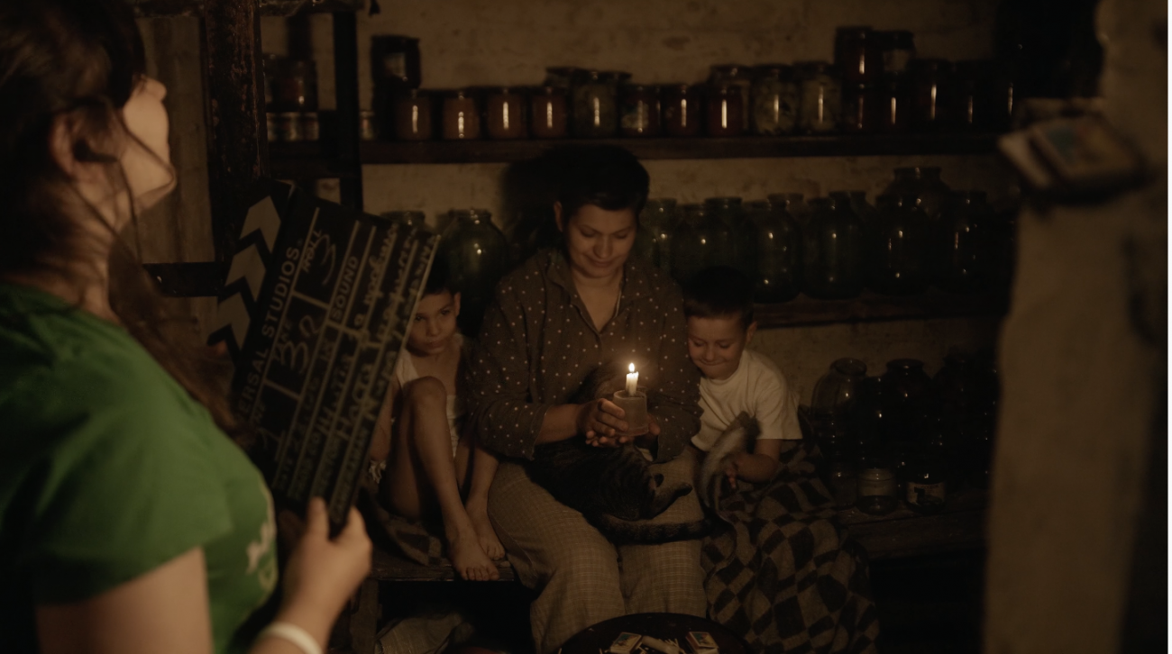 A girl in a green shirt holds a film director's slate as she prepares to film her family in their basement