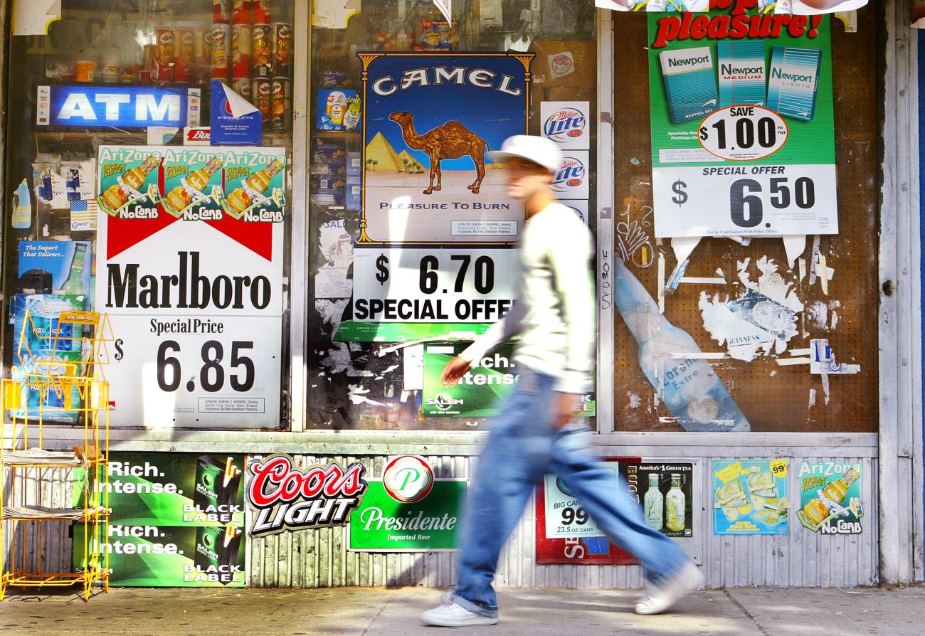 Cigarette advertisements line the wall of a supermarket as a man walks by.