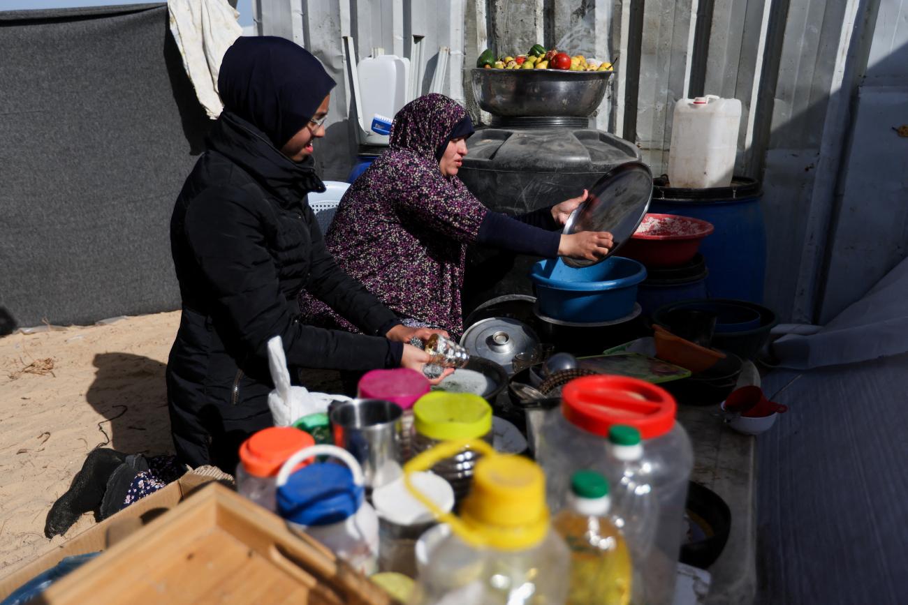 A displaced pregnant Palestinian woman washes dishes at a camp.