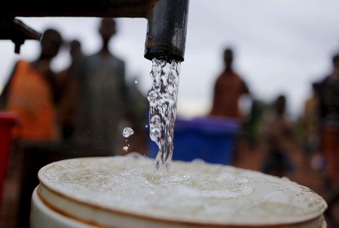 Children watch as women pump water from a borehole.