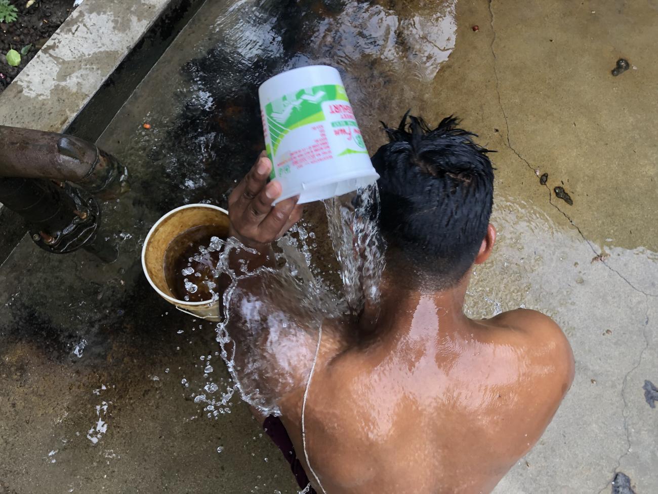 Niraj Thapa uses a bucket with yellow brown stain because of the water to take a shower, On his body are white marks he got in recent years because of fungal infections.