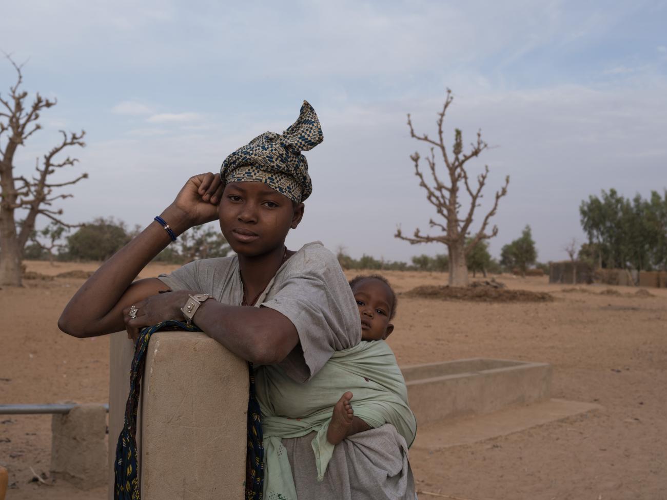 A woman stands with a baby on her back.