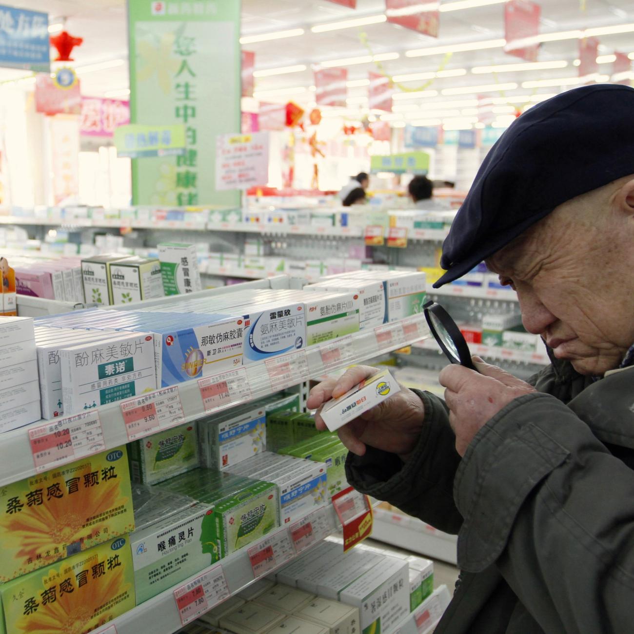 An elderly man uses a magnifier to see the descriptions on a pack of medicine at a pharmacy.