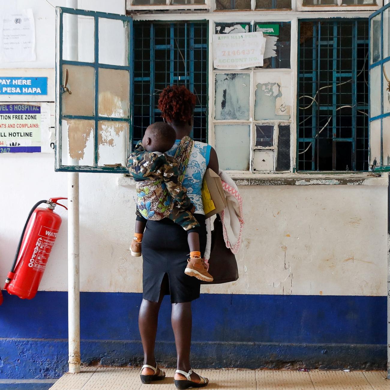 A woman carries her child as they stand at a payment counter.