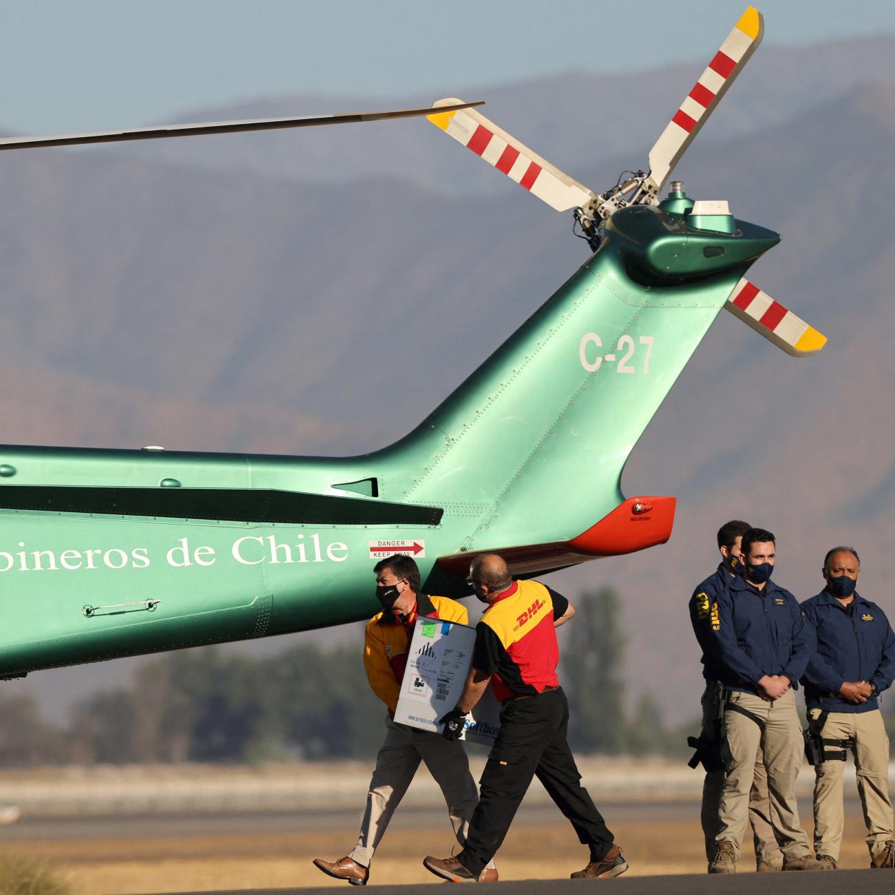 Workers carry a batch of the Pfizer-BioNTech COVID-19 vaccine to a helicopter