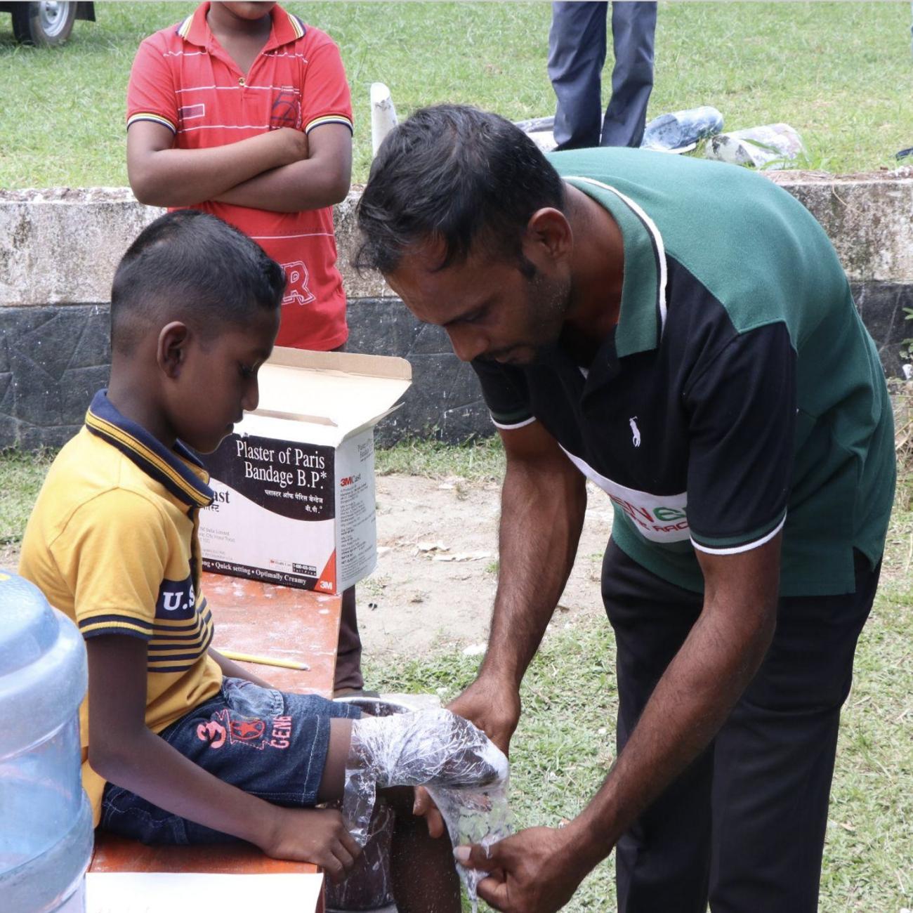 A man helps take a plaster cast of a young boy's limb.