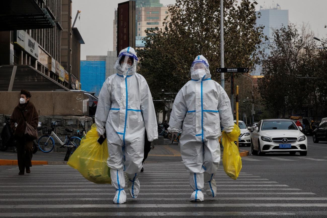 Pandemic prevention workers in protective suits cross a street as COVID-19 outbreaks continue.