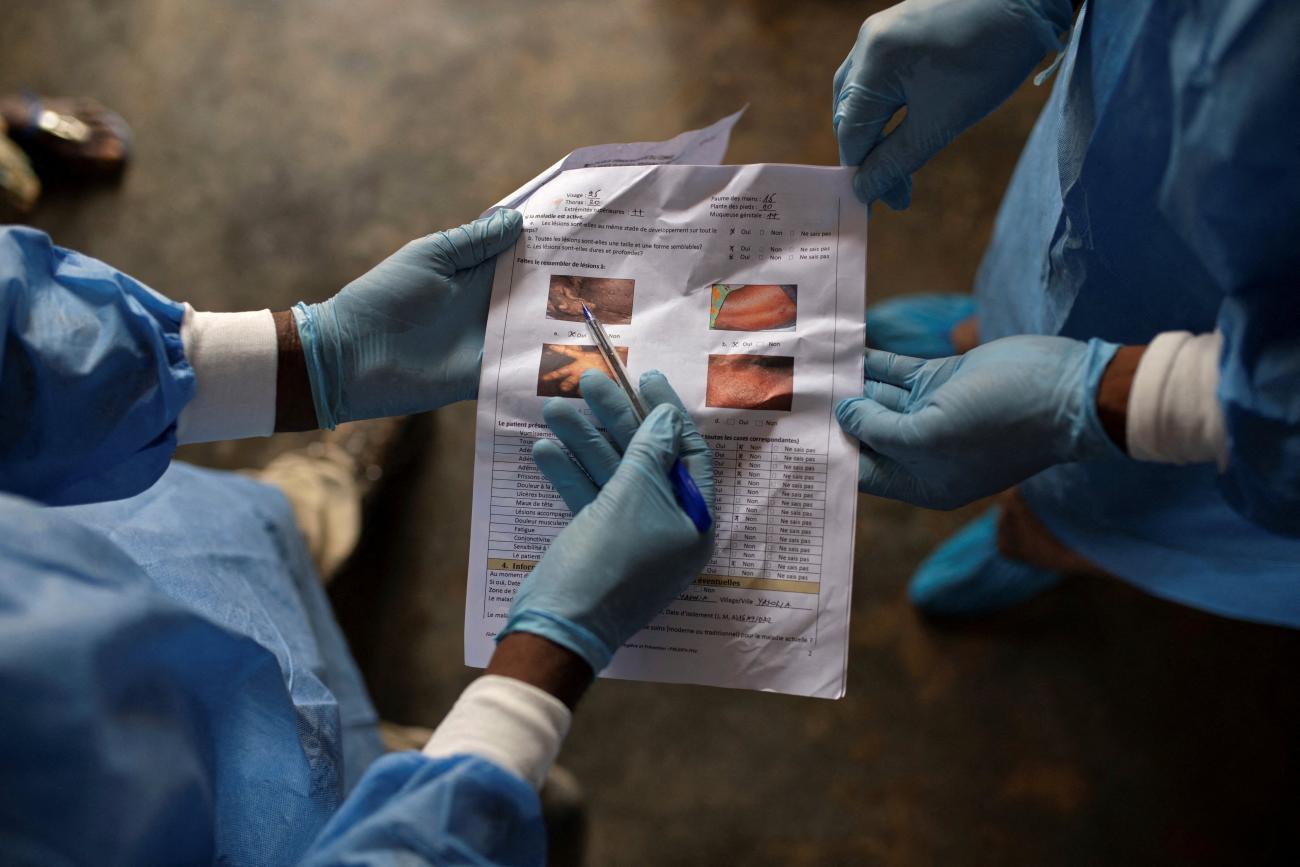 A local health official and a nurse consult documents containing information about monkeypox after taking samples from patients