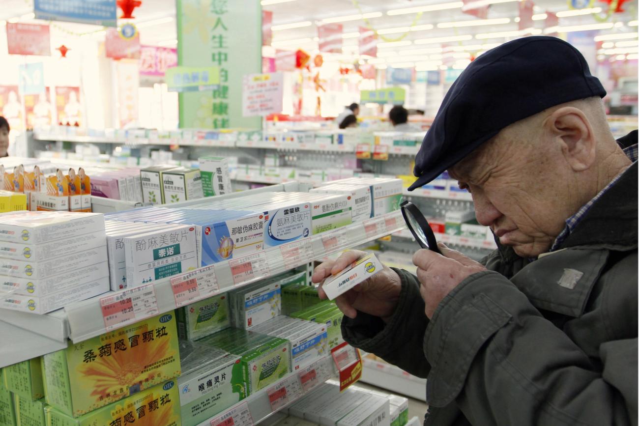 An elderly man uses a magnifier to see the descriptions on a pack of medicine at a pharmacy.