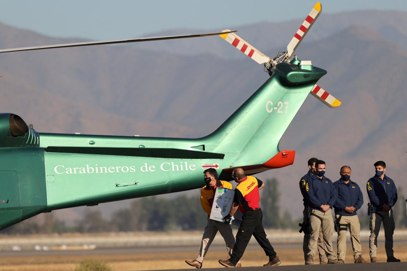 Workers carry a batch of the Pfizer-BioNTech COVID-19 vaccine to a helicopter