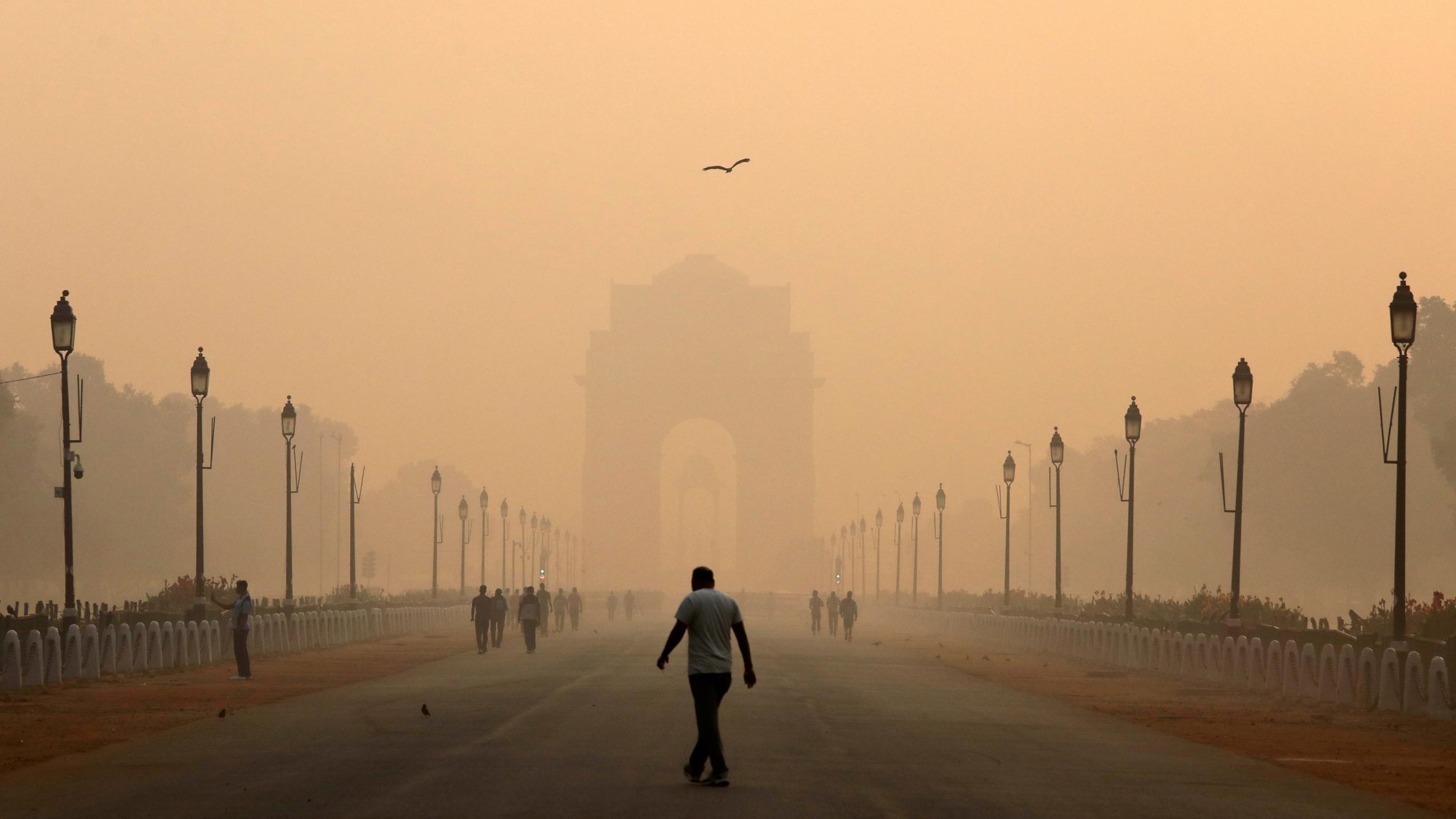 Photo shows a man in the distance and a grand architectural structure in the far distance, which is hard to see through the smog. 