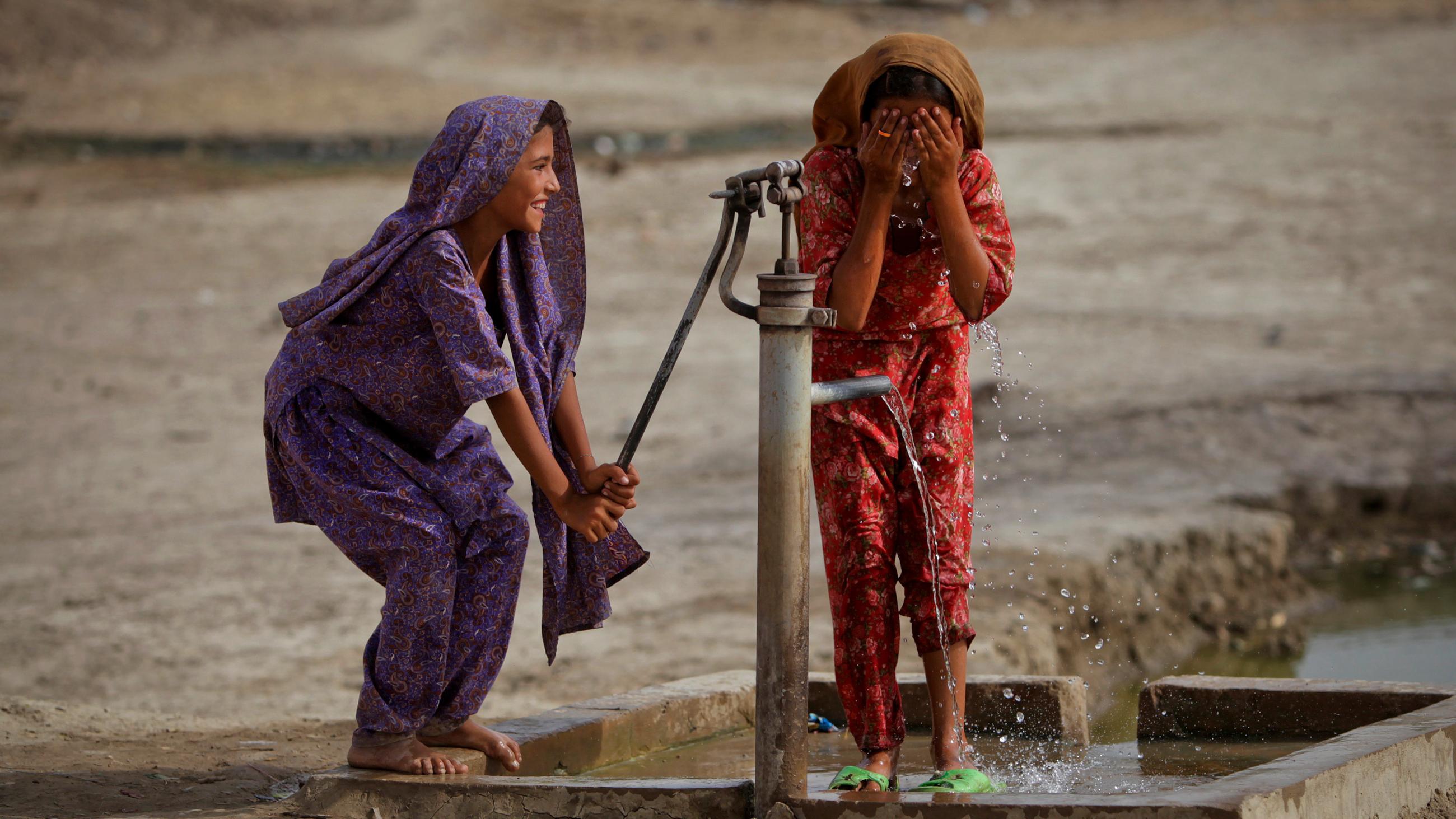 The picture shows two girls, one pumping, the other washing, and both laughing. 