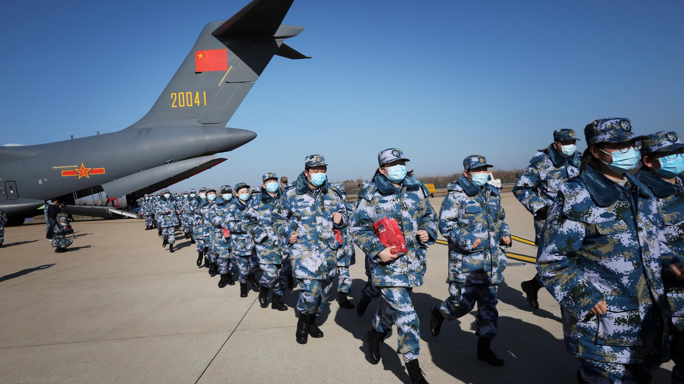 The picture shows two rows of soldiers clad in grey fatigues marching double time away from a cargo transport jet. 